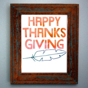 May include: A framed print with the text "HAPPY THANKSGIVING" in a gradient of orange, red, and pink. A blue and purple feather is drawn below the text.