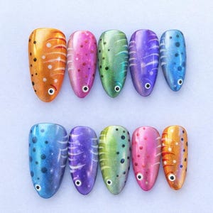 May include: Ten colorful, oval-shaped nail art designs. Each nail features a fish-like design with a painted eye and various patterns, including dots and stripes. The color palette includes orange, pink, green, purple, and blue, with a glossy finish.