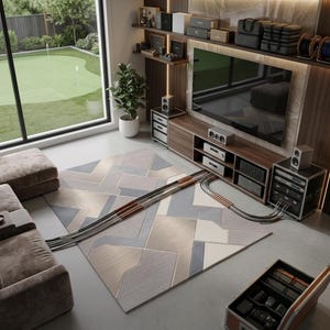 May include: A rectangular area rug featuring a geometric pattern in shades of gray, beige, and white, positioned on a concrete floor in a room with a media console, television, audio equipment, and a brown sofa, with cables running across the rug.