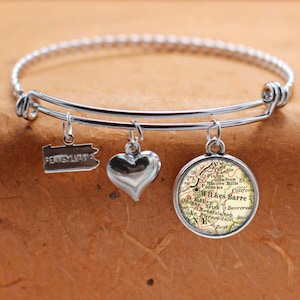May include: A silver expandable bangle bracelet with three charms: a heart, a state of Pennsylvania charm, and a round charm with a vintage map of Wilkes-Barre, Pennsylvania.