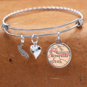 May include: Silver charm bracelet with three charms: a heart, a California outline, and a map of Riverside, California. The map charm features the text "Redlands Riverside Ana"