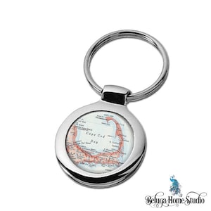 May include: A silver key chain with a round metal charm featuring a vintage map of Cape Cod Bay. The map is in shades of blue, green, and red, with the bay highlighted in red.
