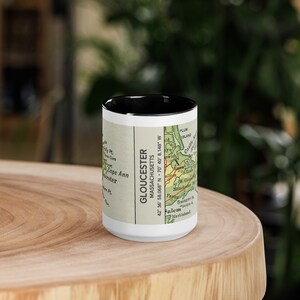 May include: A black and white vintage map mug with a black rim. The map shows the area around Gloucester, Massachusetts. The text on the mug reads "Gloucester, Massachusetts 42° 36' 58.068" N 70° 40' 8.148" W."