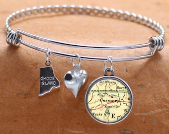 May include: A silver expandable bangle bracelet with three charms: a heart, a state of Rhode Island outline, and a round charm with a vintage map of Coventry, Rhode Island. The map shows the town's roads, landmarks, and the words "Coventry" and "Rhode Island".