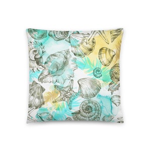 Op de afbeelding: Een wit kussen met een herhalend patroon van schelpen, zeesterren en aquarel-achtige blauwe en gele accenten.