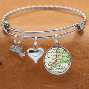 Puede incluir: Un brazalete de plata con tres dijes: un corazón, un contorno del estado de Massachusetts y un dije redondo con un mapa vintage de Falmouth, Massachusetts.