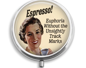 Puede incluir: Una caja de píldoras redonda de color plateado con una tapa blanca. La tapa presenta un anuncio vintage de espresso con una mujer sosteniendo una taza de café. El texto dice "Espresso! Euforia sin las marcas antiestéticas."