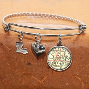 May include: A silver charm bracelet with three charms: a heart, a map of Monroe, Louisiana, and the state of Louisiana.
