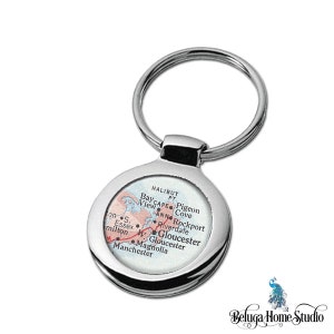 May include: A silver key chain with a round, white, and red map of Gloucester, Massachusetts. The map shows the location of Halibut Point, Bay View, Pigeon Cove, Ann, Rockport, Riverdale, Gloucester, and Manchester.