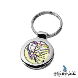 May include: A silver keychain with a round, silver-rimmed image of a vintage map of Pulaski County, Illinois. The map is in shades of yellow, pink, and green. The text "PULASKI" is visible on the map.