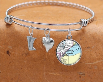 May include: A silver charm bracelet with three charms: a heart, a state of Minnesota outline, and a vintage map of Duluth, Minnesota. The map charm features the text "DULUTH-LA Superior".