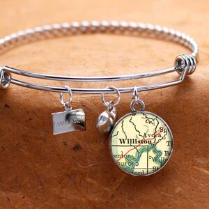 Puede incluir: Un brazalete expandible de plata con múltiples encantos. Un encanto es un pequeño corazón de plata, otro es un encanto de plata con el texto "South Dakota" y el encanto final es un encanto redondo de vidrio con un mapa vintage de Williston, Dakota del Norte.