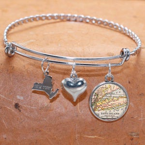 May include: A silver charm bracelet with three charms: a heart, a map of Long Island, and the outline of New York State. The bracelet is made of a braided metal band.