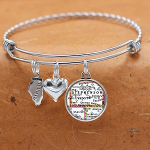 May include: A silver charm bracelet with three charms: a heart, a state of Illinois outline, and a map of Stephenson, Illinois. The map charm features the text "Stephenson" and "Freeport".