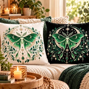 May include: Two square throw pillows featuring a central green moth illustration surrounded by a crescent moon, stars, and botanical elements. One pillow has a white background, while the other has a black background, both displaying identical intricate designs.