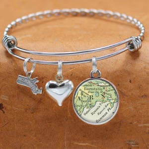 Puede incluir: Un brazalete de plata con tres dijes: un corazón, un mapa de Cape Cod, Massachusetts, y un pequeño contorno del estado de Massachusetts.