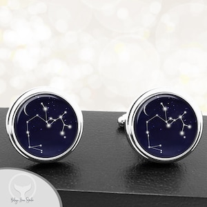 May include: A pair of silver cufflinks with a dark blue background and a white outline of the Sagittarius constellation.