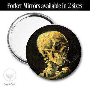 Könnte beinhalten: Ein runder Taschenspiegel mit silbernem Rahmen und schwarzem Hintergrund. Der Spiegel zeigt ein Gemälde eines gelben Schädels mit einer Zigarette im Mund.