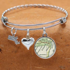 Puede incluir: Un brazalete de plata con tres dijes: un corazón, un mapa de Cape Cod, Massachusetts, y el estado de Massachusetts. El dije del mapa muestra las ciudades de Harwich, Harwich Port, Chatham y la isla Monomoy.