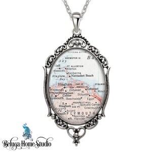 May include: A silver pendant necklace featuring a vintage map of Hingham, Massachusetts. The map is surrounded by an ornate silver frame with a heart-shaped bail.