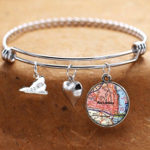 Puede incluir: Un brazalete expandible de plata con tres dijes: un corazón, un contorno plateado del estado de Virginia y un dije redondo con un mapa de Alexandria, Virginia.