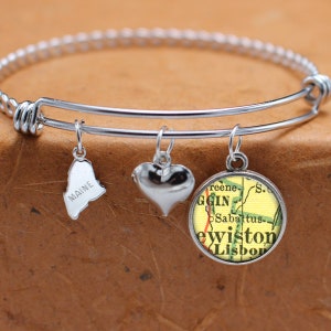 May include: A silver expandable bracelet with three charms: a heart, a map of Maine, and a map of Lewiston, Maine. The map charms are in a circular glass frame.