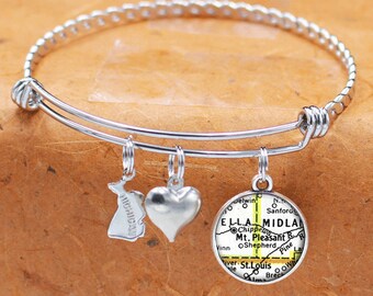 May include: A silver expandable bangle bracelet with three charms. The charms are a heart, a state outline of Michigan, and a round charm with a map of Ella, Michigan.