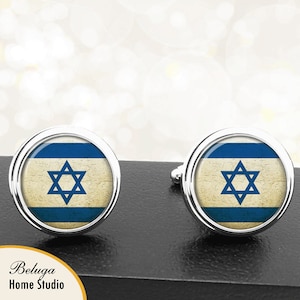 May include: A pair of silver cufflinks with a round, blue and white design featuring the Israeli flag. The flag has a blue Star of David on a white background with two blue stripes.