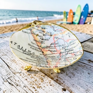 May include: A decorative seashell dish featuring a decoupage map of the Southern California coastline, including San Diego and Oceanside. The shell has a gold-painted rim and rests on three small gold-toned metal feet, displaying detailed cartographic text.