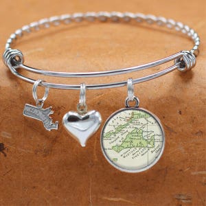 May include: A silver bangle bracelet with three charms: a heart, a small outline of Massachusetts, and a round charm with a vintage map of Martha's Vineyard.