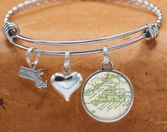 May include: A silver bangle bracelet with three charms: a heart, a small outline of Massachusetts, and a round charm with a vintage map of Martha's Vineyard.