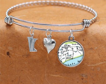 May include: A silver charm bracelet with three charms: a heart, a state of Minnesota outline, and a map of the Upper Peninsula of Michigan. The map charm has the text "Eagle Mtn. 301 0 MISQUAH HILLS /Grand Marais South Fo 0 Min GRAND Lake No" on it.