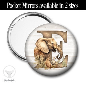May include: A round pocket mirror with a silver metal frame. The mirror's design features a watercolor illustration of an elephant, a bird, and the letter "E" on a white wood-grain background. The text "Pocket Mirrors available in 2 sizes" is at the top.