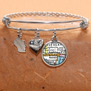 Puede incluir: Un brazalete de plata con tres dijes: un corazón, un contorno del estado de Wisconsin y un mapa del área del condado de Outagamie en Wisconsin.