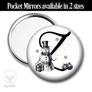 May include: A white round compact mirror with a snowman and the letter Z in black. The snowman is wearing a black top hat and a black scarf. The background is white with a silver glitter effect.