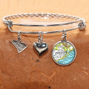 May include: A silver bangle bracelet with three charms: a heart, a state outline of South Carolina, and a map of Charleston, South Carolina.