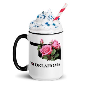 May include: White ceramic mug with a black handle and rim. The mug features a black outline of the state of Oklahoma with pink roses inside. The text "I love Oklahoma" is printed below the state outline.