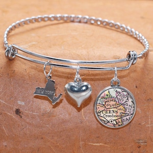 Puede incluir: Un brazalete de plata con tres dijes: un corazón, un mapa de Queens, Nueva York, y el contorno del estado de Nueva York.