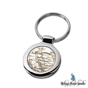 May include: A silver keychain with a round, silver-colored charm featuring a vintage map of the San Francisco Bay Area. The map shows the cities of Vallejo, Richmond, Berkeley, Oakland, San Francisco, and Fremont.