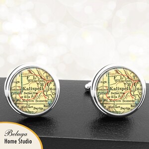 May include: A pair of silver cufflinks featuring a vintage map of Kalispell, Montana. The map is in shades of yellow, green, and red, with the city name highlighted in black.