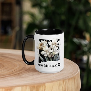 May include: White ceramic mug with a black rim and handle. The mug features a black and white illustration of a flower with the text "NEW MEXICO" and a heart symbol.