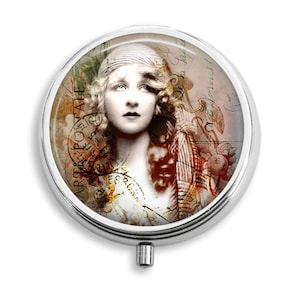Op de afbeelding: Een ronde zilveren compact spiegel met een vintage-geïnspireerd ontwerp. De afbeelding toont een vrouw met een hoofddoek en een achtergrond van oude brieven en postzegels. De tekst op de postzegels luidt "Art. Postale".