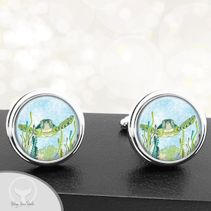 May include: A pair of silver cufflinks with a round, blue, green, and white design featuring a sea turtle swimming in a coral reef.