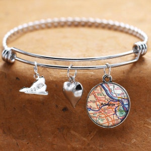 Puede incluir: Un brazalete expandible de plata con tres dijes: un corazón, un mapa de Arlington, Virginia, y el contorno del estado de Virginia con la palabra "Virginia" inscrita en él.