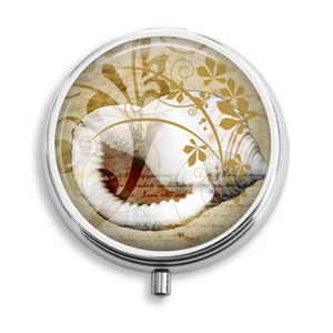 May include: A round silver compact with a hinged lid. The lid features a seashell with a brown and white pattern on a background of gold and brown floral designs.