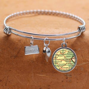 May include: A silver charm bracelet with three charms: a heart, a state of Kansas charm, and a round charm with a vintage map of Atchison, Kansas.