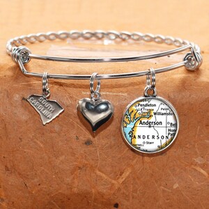 May include: Silver charm bracelet with three charms: a heart, a map of South Carolina, and a map of Anderson, South Carolina.