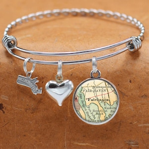 May include: A silver expandable bracelet with three charms: a heart, a state of Massachusetts charm, and a round charm with a vintage map of Fairhaven, Massachusetts.
