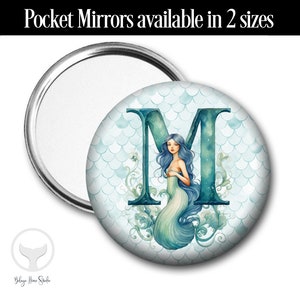 May include: A round pocket mirror with a mermaid illustration on the front. The mermaid is blue and green and is sitting inside the letter "M". The background is a light blue with a pattern of scales.