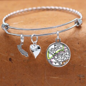 May include: A silver bangle bracelet with three charms: a heart, a California outline, and a round charm with a map of Modesto, California. The map features the names of surrounding towns and cities.